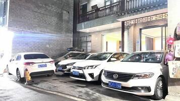 A parking area with multiple white cars parked in front of a building with a brick facade and a balcony.