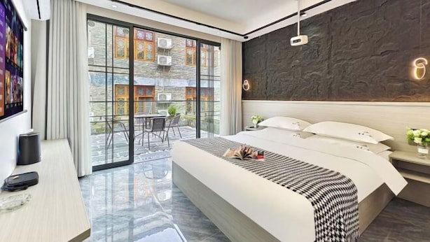 Een moderne hotelkamer met een groot bed, een bureau, een televisie en een balkon met uitzicht op gebouwen.