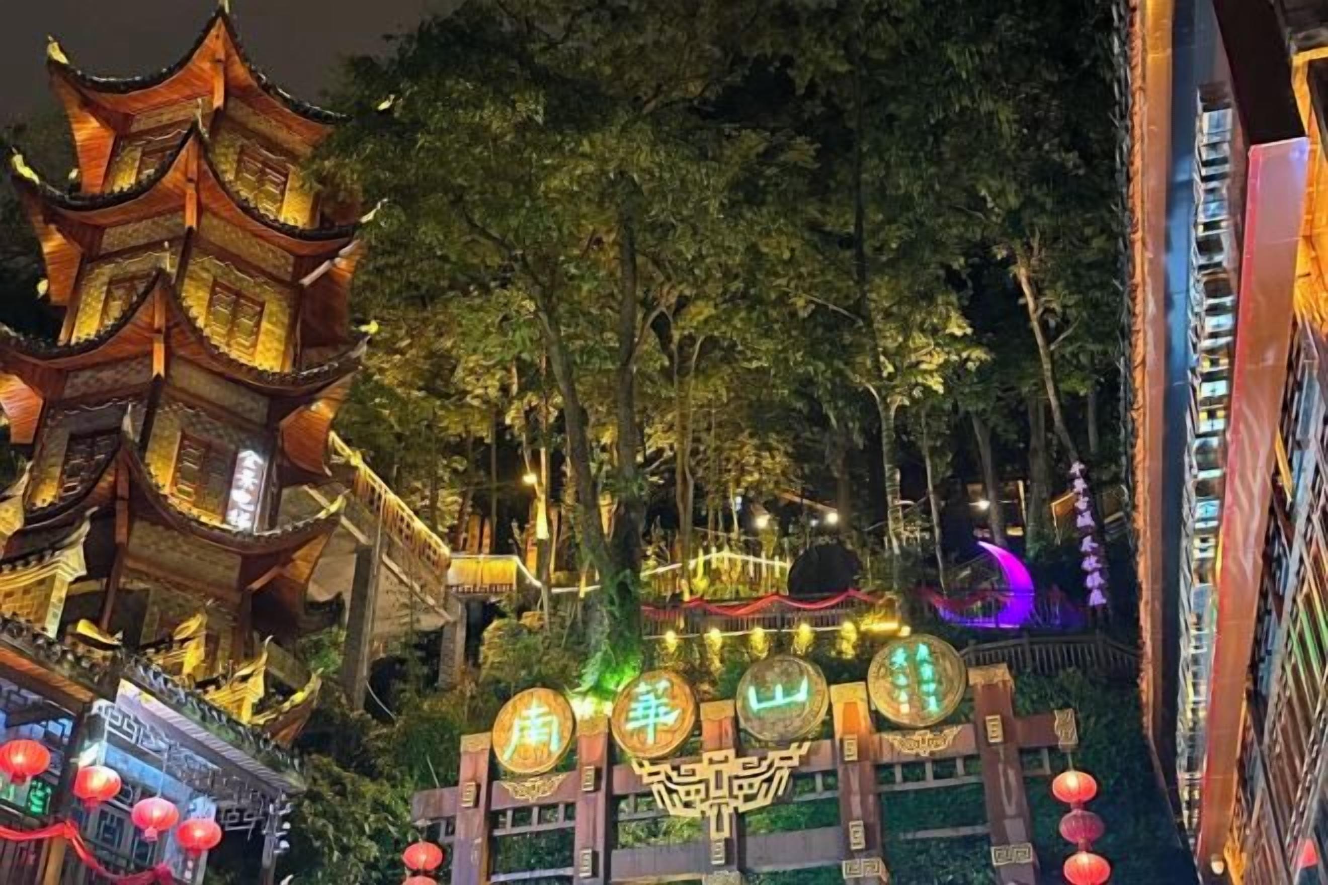 A traditional pagoda-style building with multiple tiers, surrounded by trees and illuminated by warm lighting.