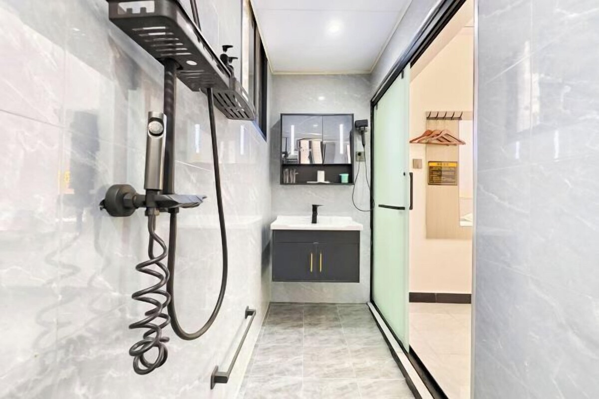 A modern bathroom with a marble floor, a black and white vanity, and a glass shower enclosure.