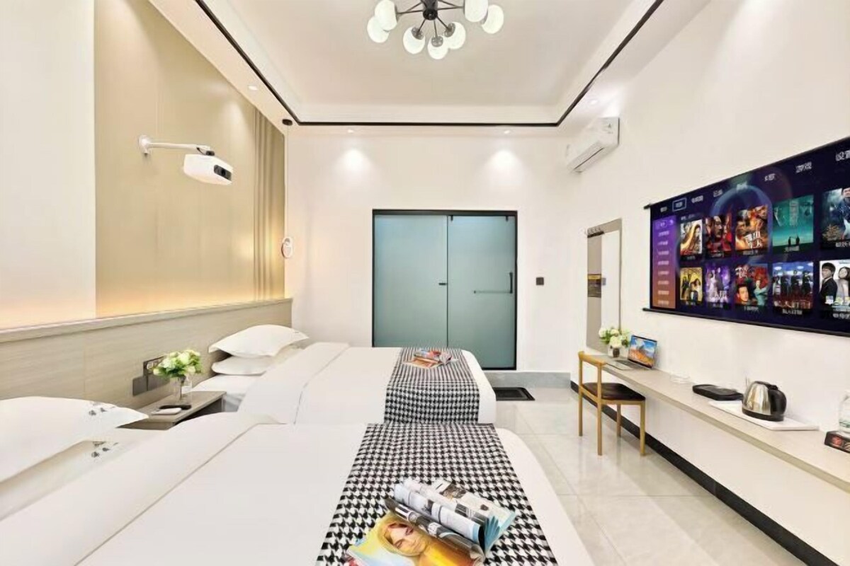 A modern hotel room with a bed, bedside table, wall-mounted TV, and a large window.