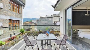 Een balkon met een tafel en stoelen, een bed met een wit hoofdeinde en uitzicht op traditionele gebouwen.