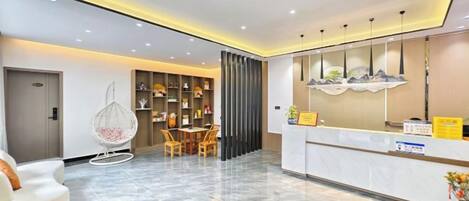 Zona de recepción de hotel con piso de mármol, mostrador de recepción, área de asientos con sillas y una pared decorativa.