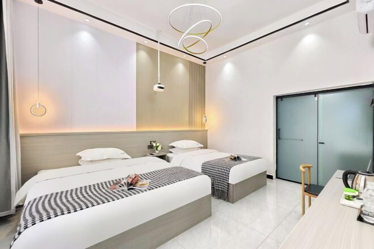 A modern hotel room with two beds, a desk, and a wardrobe.