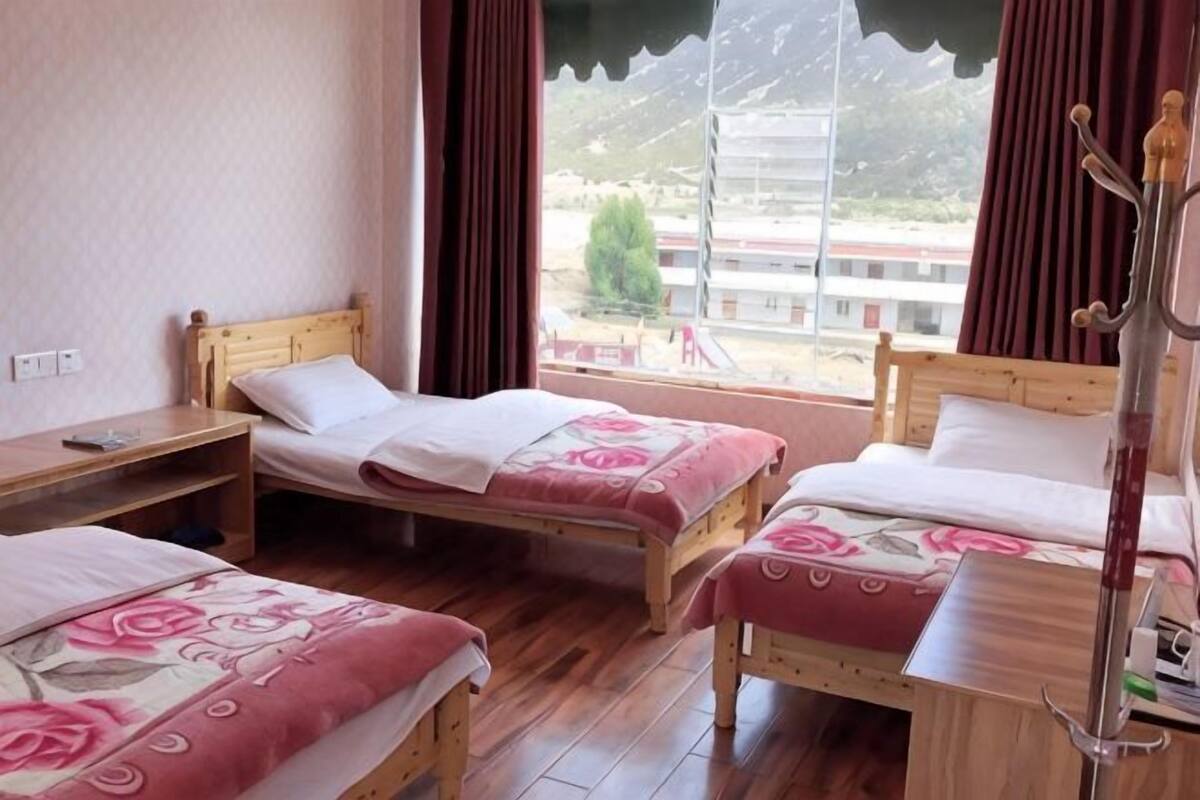 A room with three wooden beds, a window with curtains, and a view of a building outside.