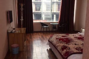 Habitación de hotel con cama, escritorio, silla, mesita y ventana con cortinas.
