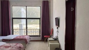 Habitación de hotel con dos camas, un escritorio, una silla, un televisor y una ventana con cortinas.