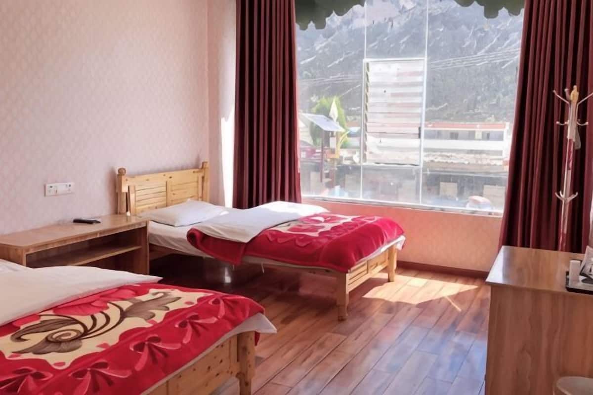 A room with two wooden beds, a wooden desk, a window with curtains, and a view of buildings outside.