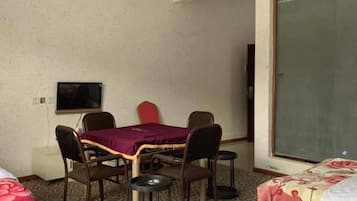 A room with a bed, a table with chairs, a television, and a sliding door.