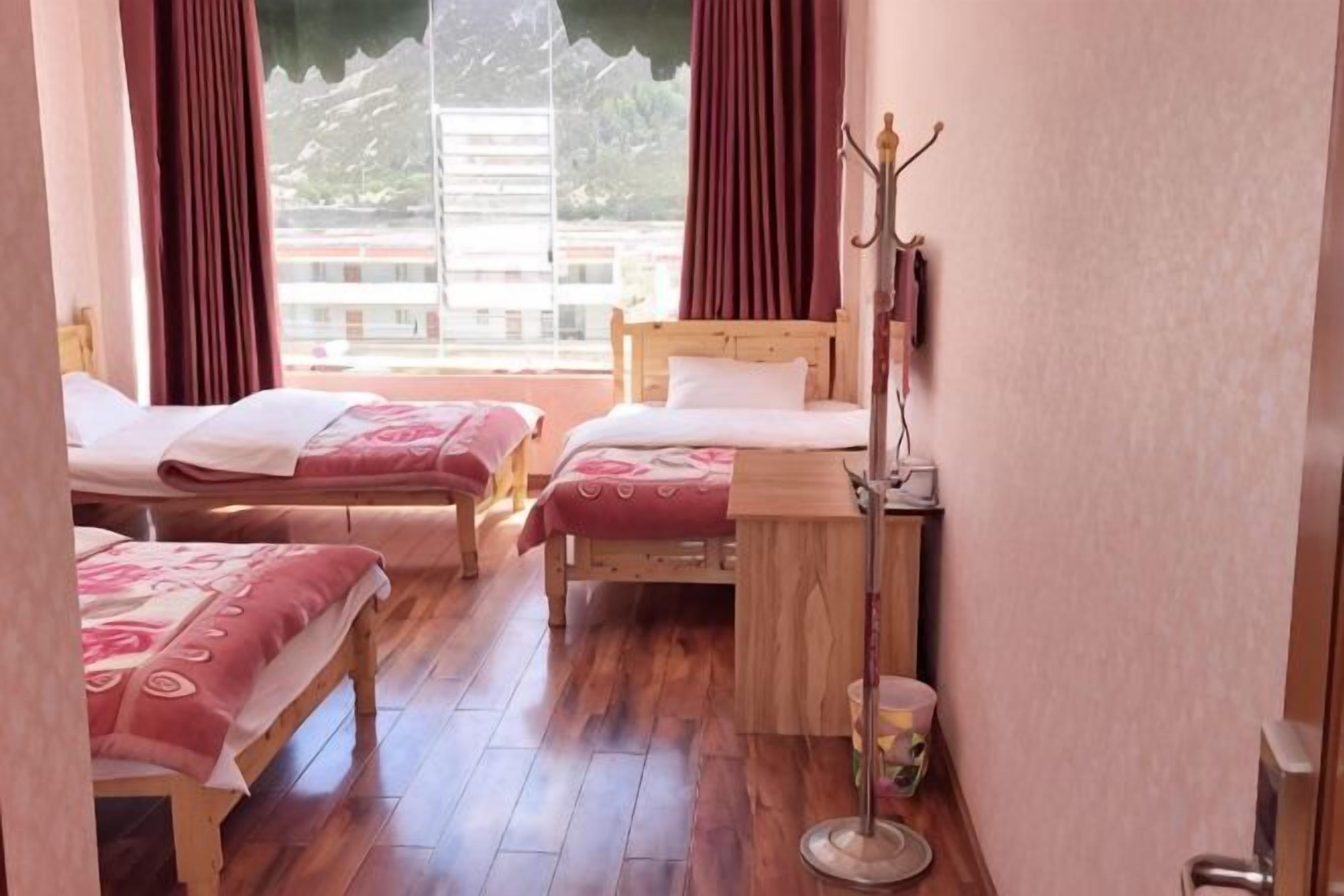 A room with two beds, a wooden floor, a coat rack, and a window with curtains.