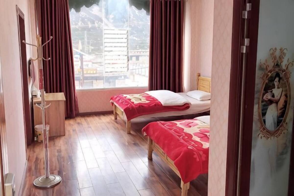 A bedroom with two beds, a window with curtains, a coat rack, and a framed picture on the wall.