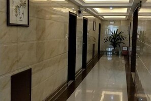 A hallway with marble walls, black doors, and a plant in the center. - Jinhui Hotel (Yangjiang)