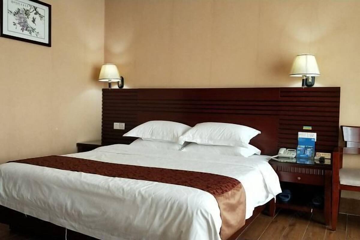 A hotel room with a bed, two bedside lamps, a nightstand with a phone and a magazine, and a framed picture on the wall.