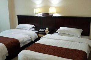 A hotel room with two single beds, each with white linens and brown bedspreads. There are two bedside lamps on a nightstand between the beds.