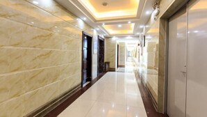 A corridor with marble walls and a shiny tiled floor, leading to a door with a dark frame. - Jinhui Hotel (Yangjiang)