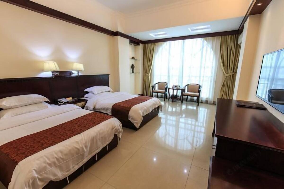 A hotel room with two beds, a desk, a chair, and a TV.