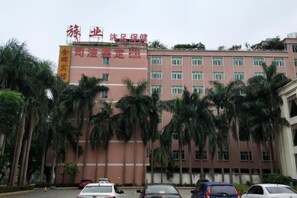A multi-story building with a red facade, palm trees in front, and several parked cars.
