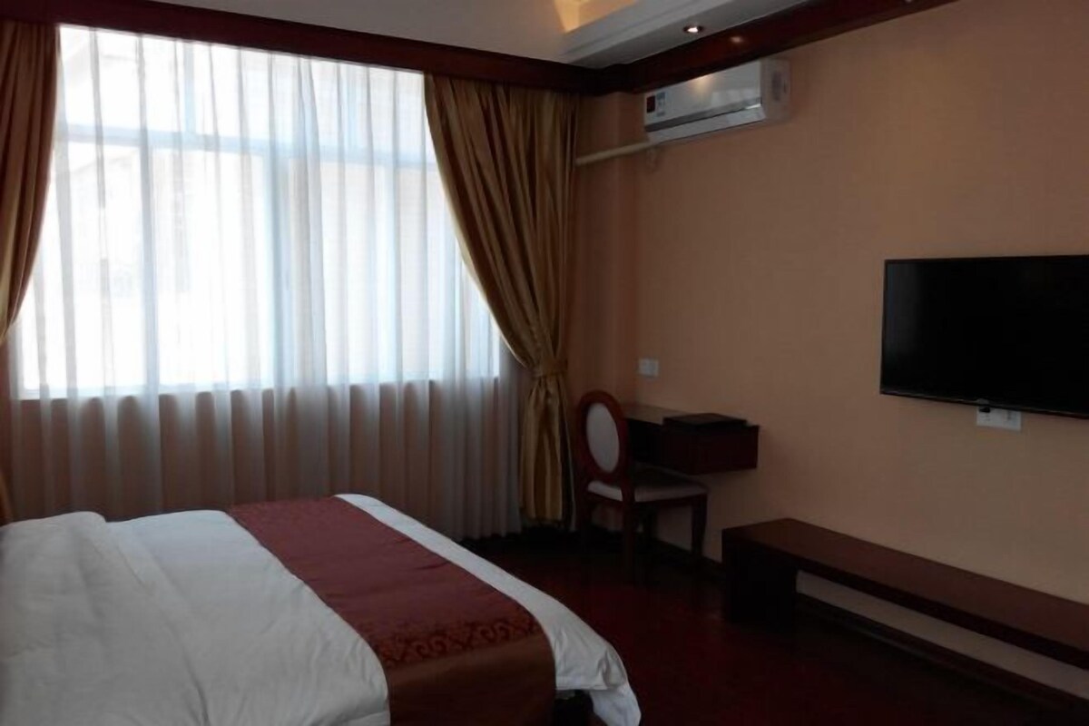 Quarto de hotel com cama, televisão, escrivaninha e cadeira.