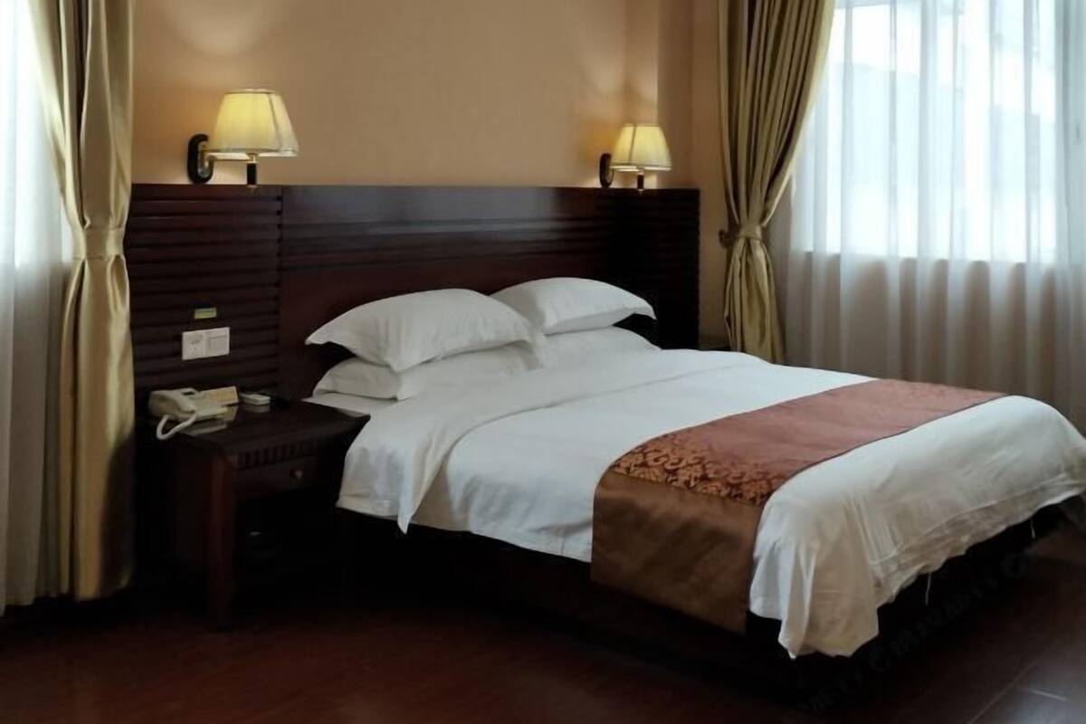 A hotel room with a wooden headboard, two bedside lamps, a telephone, and a bed with white linens and a brown throw blanket.