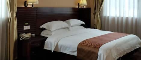 Habitación de hotel con cabecera de madera, dos lámparas de noche, un teléfono y una cama con ropa blanca y una manta marrón.