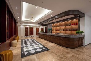 Un vestíbulo de hotel con mostrador de recepción, piso a cuadros y un diseño moderno en el techo.