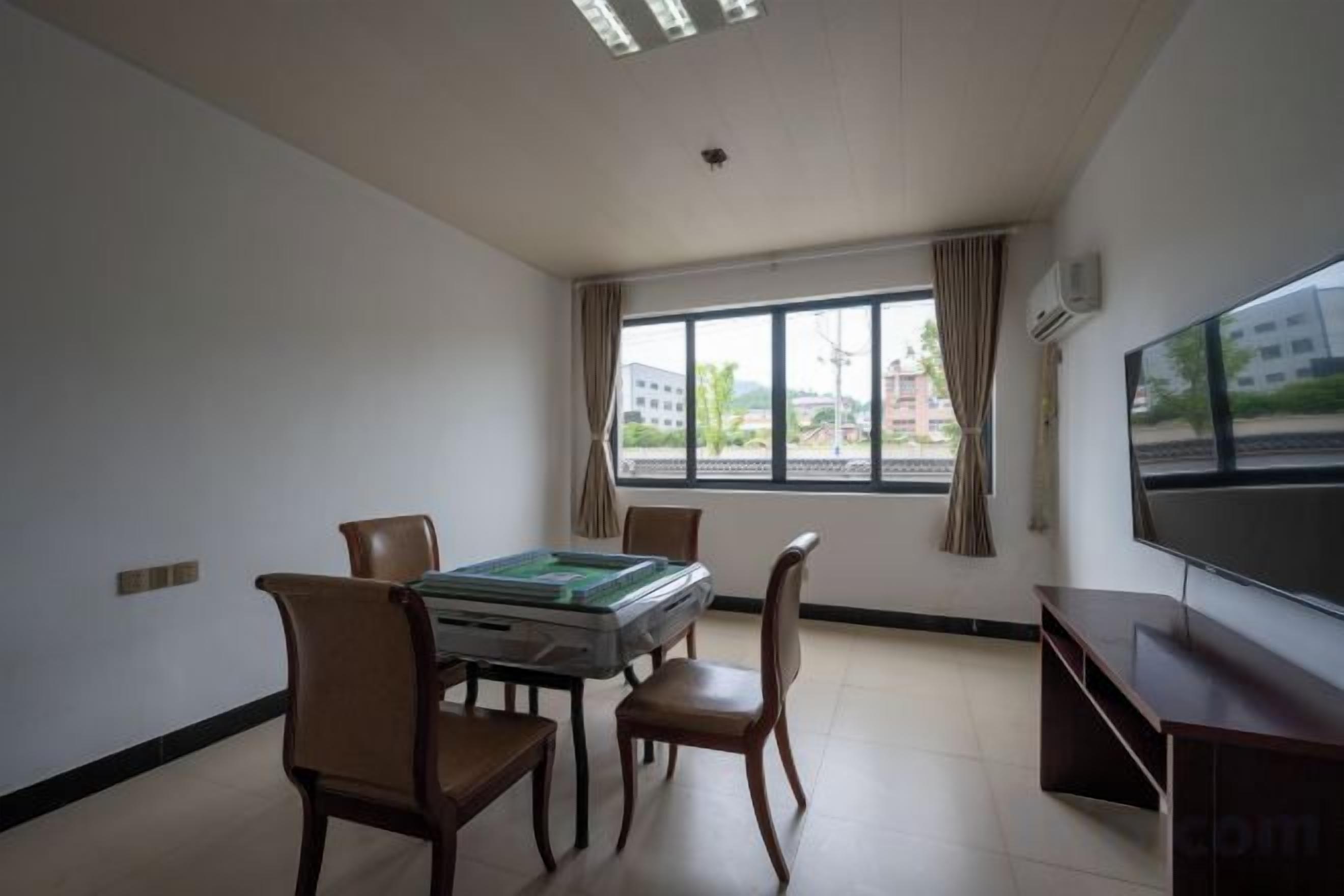 A room with a table, chairs, a flat-screen TV, and a window with curtains.