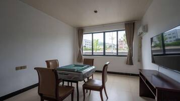 A room with a table, chairs, a flat-screen TV, and a window with curtains.
