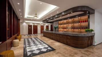 A hotel lobby with a reception desk, a checkered floor mat, and a ceiling light fixture.