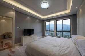 Ein Schlafzimmer mit einem großen Bett, einem Fernseher auf einer weißen Kommode, einem Fenster mit Blick auf die Berge und einer Deckenleuchte.