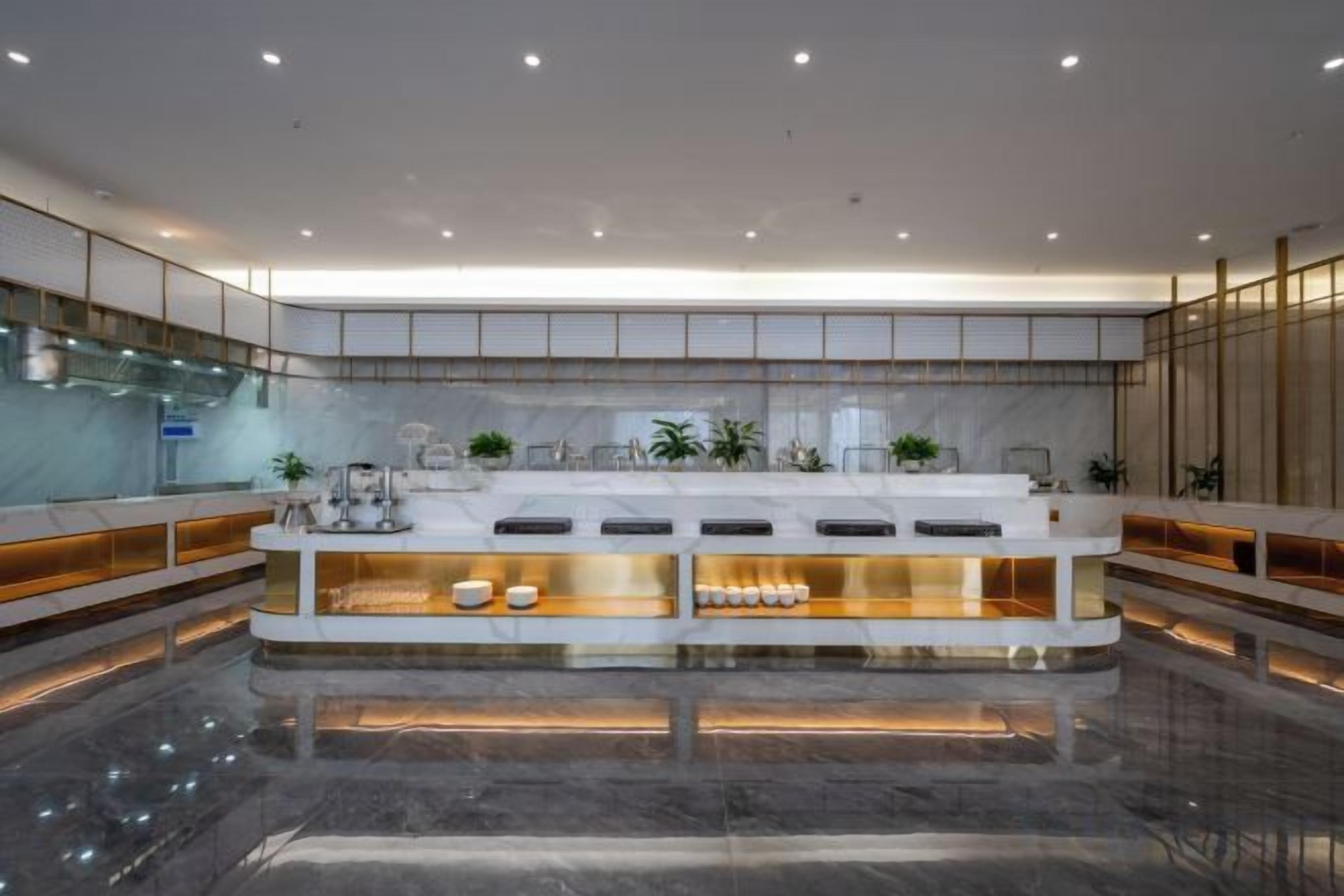 A modern hotel lobby with a central reception desk, marble flooring, and a glass partition.