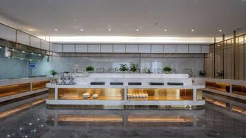 A modern hotel lobby with a central reception desk, marble flooring, and a glass partition.