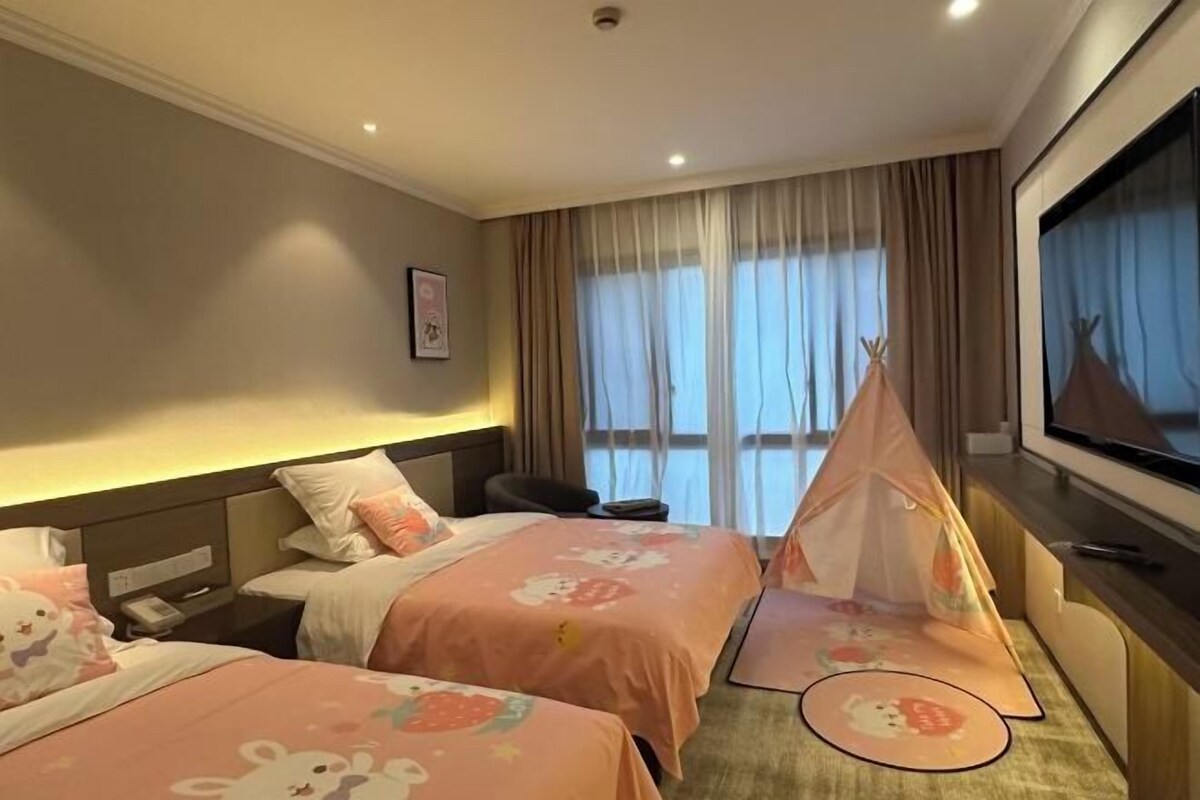 Ein Hotelzimmer mit zwei Betten, einem Fernseher, einem Fenster mit Vorhängen und einem Zelt auf dem Boden.