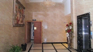 A lobby with a chandelier, a framed painting, a wooden door, and a floral arrangement.