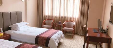 Une chambre d’hôtel avec deux lits, un bureau, deux chaises et une fenêtre avec des rideaux.
