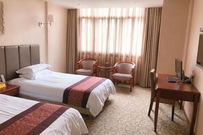 Ein Hotelzimmer mit zwei Betten, einem Schreibtisch, einem Stuhl, einem kleinen Tisch und einem Fenster mit Vorhängen.