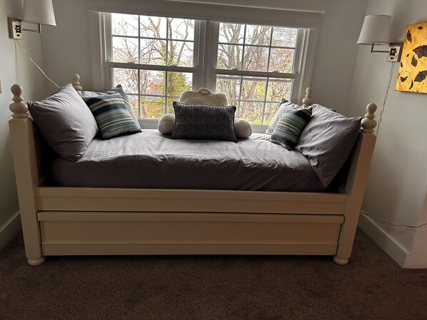A bed with a headboard, a window with a view of trees, and a lamp on the wall.