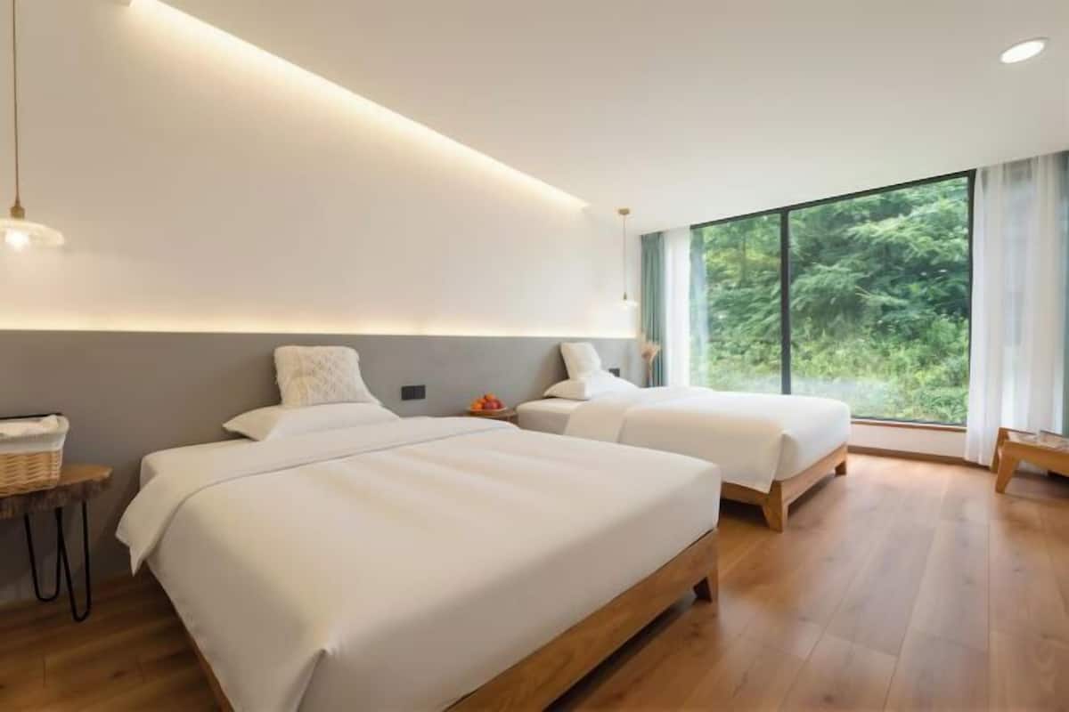Una habitación de hotel moderna con dos camas, un ventanal grande y suelo de madera.