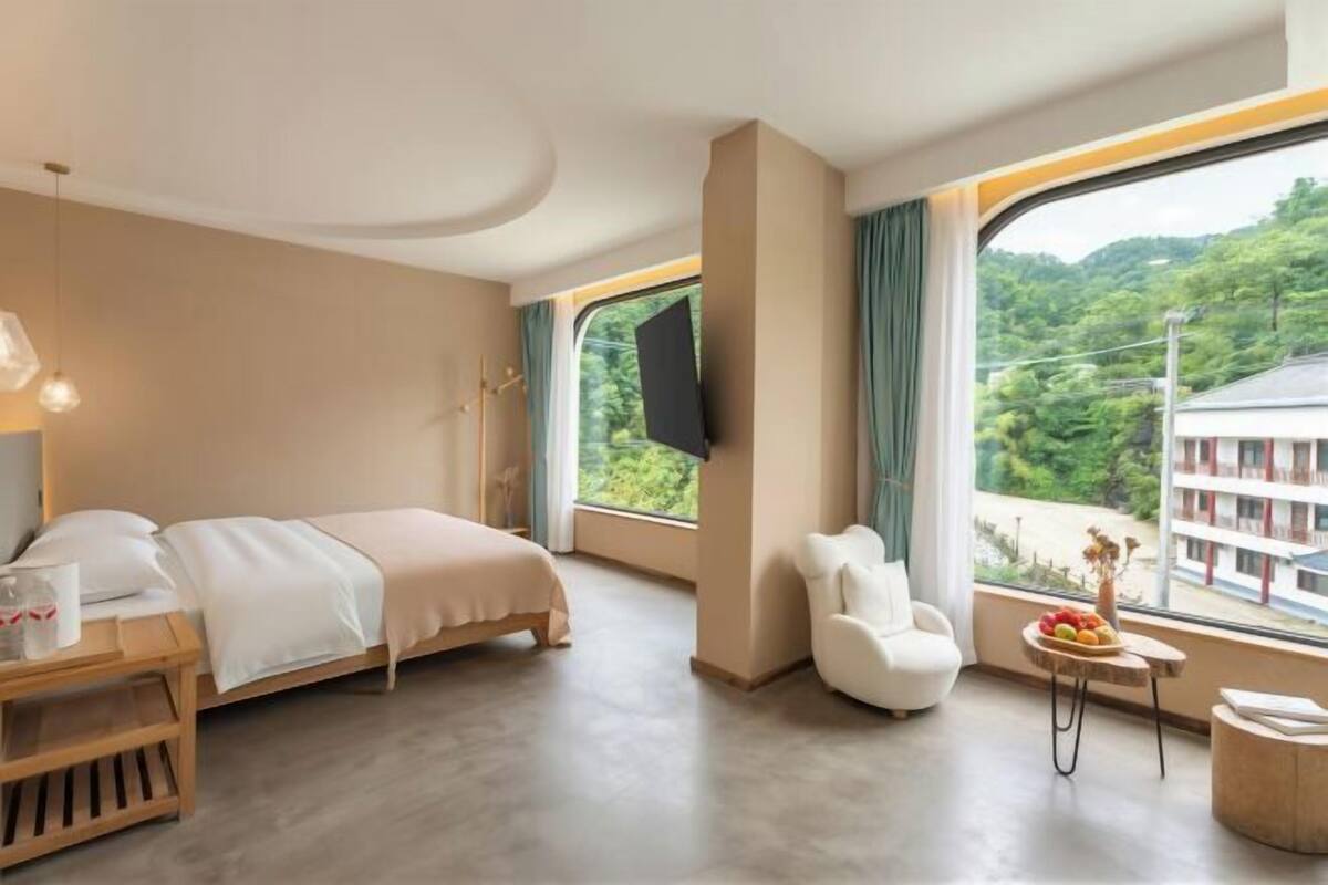 Habitación de hotel moderna con una cama grande, televisión, una pequeña mesa con frutero y vistas a zonas verdes.