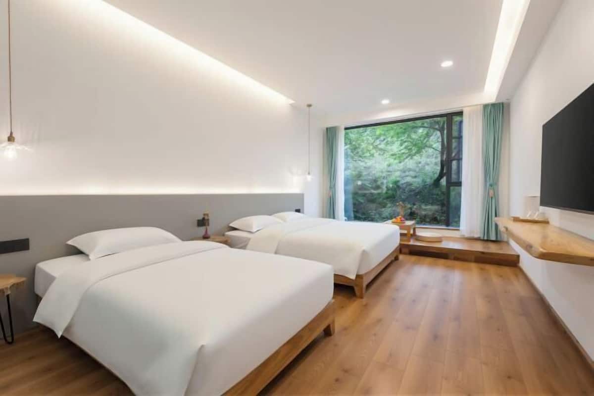 Una habitación de hotel moderna con dos camas, televisión y ventana con vistas a zonas verdes.