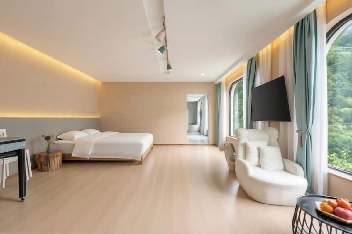 Una habitación de hotel moderna con cama, zona de estar, televisor y ventanas amplias.