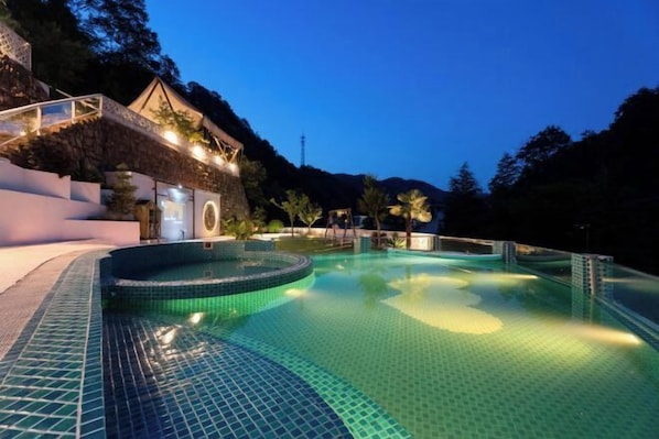 A swimming pool with a tiled edge, surrounded by a stone wall and a building with a balcony. - Chongdugou Mochi B & B (Luanchuan)