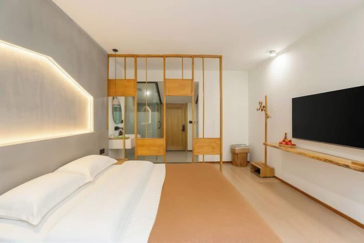 Una habitación de hotel moderna con cama, televisor, separador de madera y espejo.