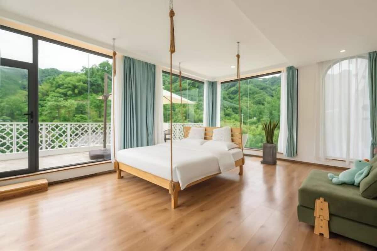 Un dormitorio amplio con una cama grande, un balcón y vistas a zonas verdes.