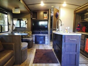 Een compact RV-interieur met een kitchenette, zithoek en televisie.