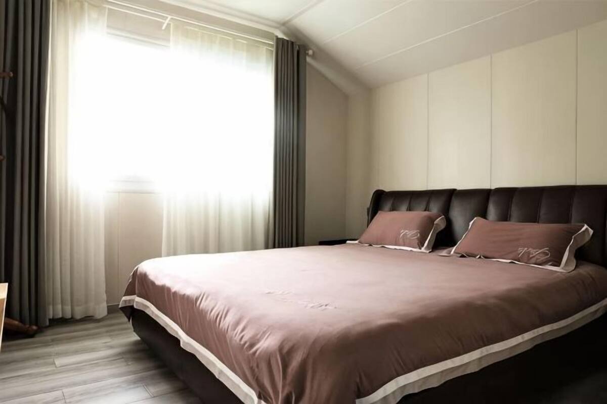 Un dormitorio con una cama grande, cabecera y ventana con cortinas.