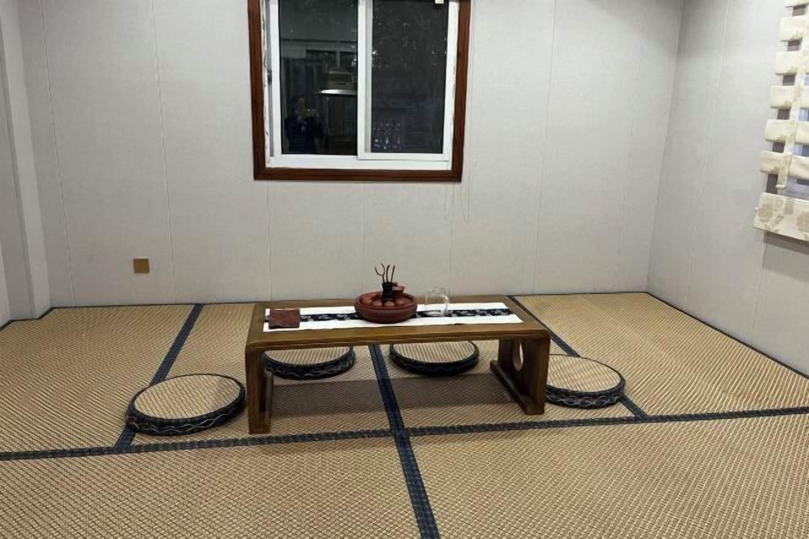 Una habitación con suelo de tatami, una mesa de madera baja, una ventana y un estante en la pared.