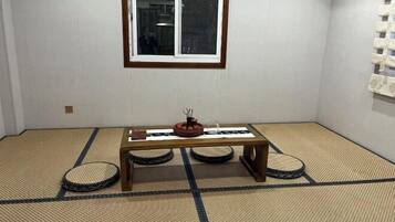 Una habitación con suelo de tatami, una mesa de madera baja, una ventana y un estante en la pared.