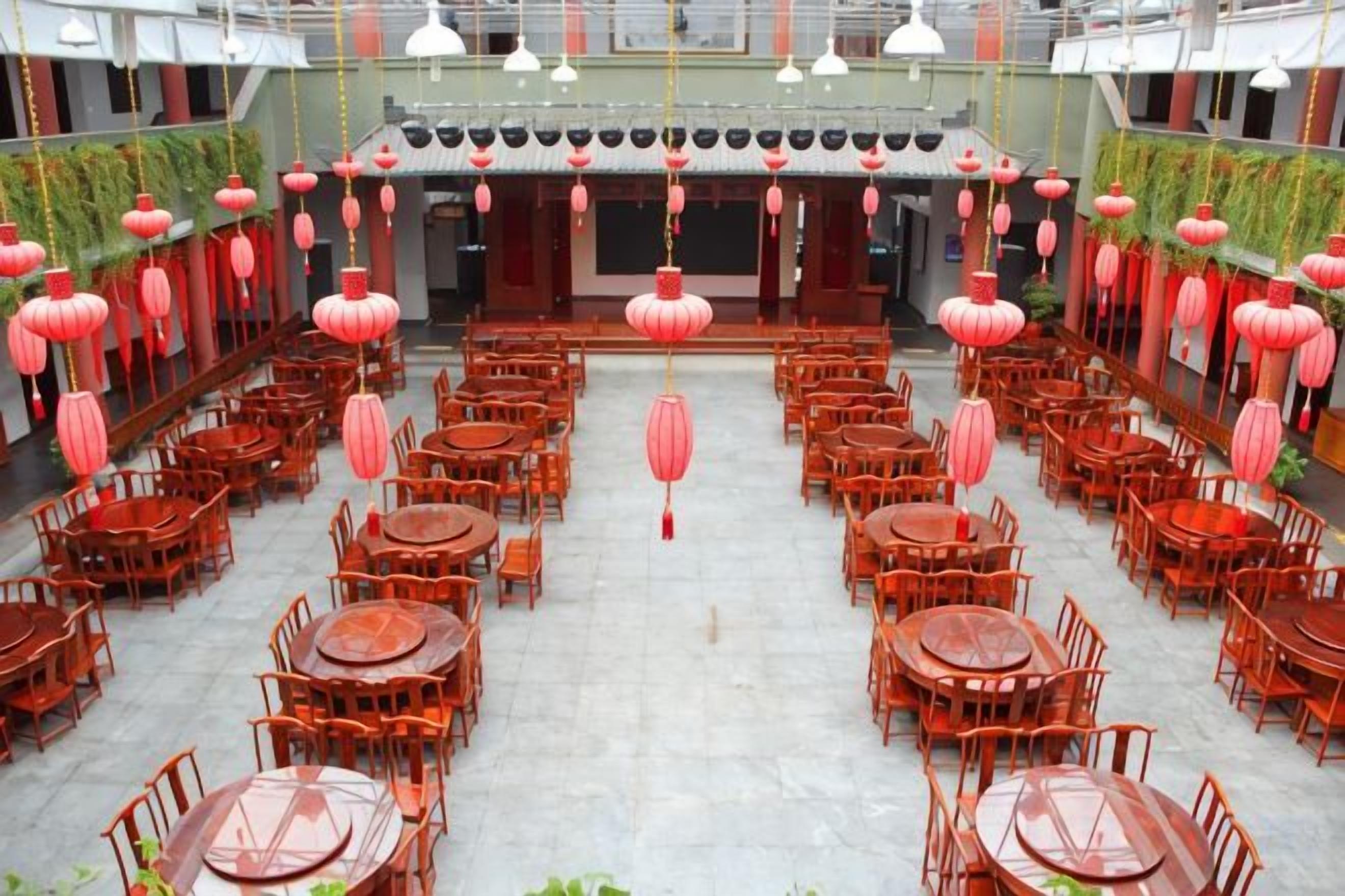 A spacious indoor dining area with multiple round tables and chairs, red lanterns hanging from the ceiling, and a central walkway.