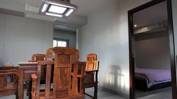 Una habitación con una mesa de madera y sillas, una cama con un edredón morado y una puerta que da a otra habitación.