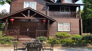 Una casa de madera de dos pisos con un balcón, un porche delantero con una mesa y sillas, y faroles rojos.